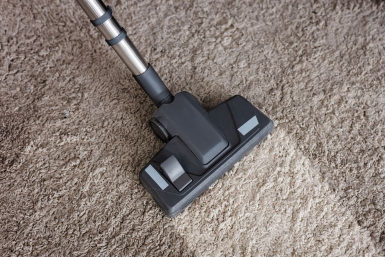 A vacuum cleaner head moving over a textured brown carpet, leaving a clean, lighter-colored stripe behind.