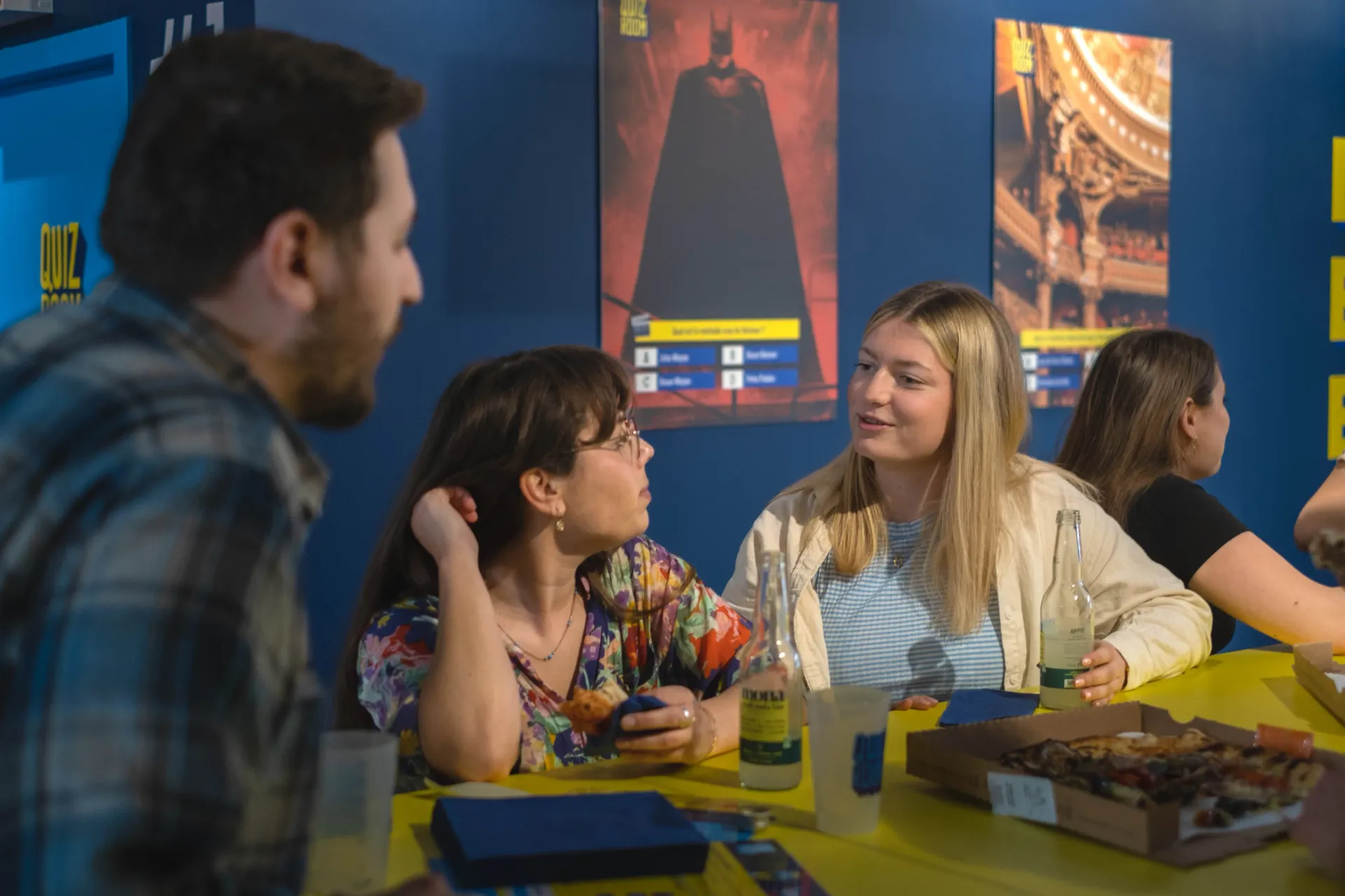 Woman with tiara laughs, illuminated by spotlight. Others in white shirts are blurred in the background.