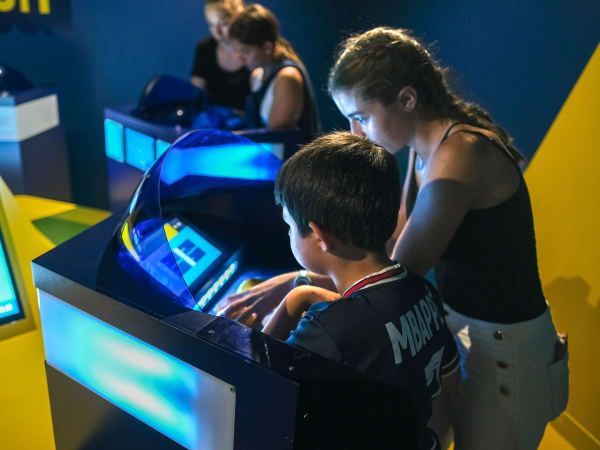 Boy and girl looking at a blue screen display in a science center exhibit. Other people in background.