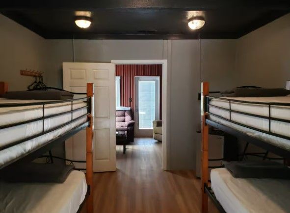 A room with four bunk beds and a door leading to a living room.