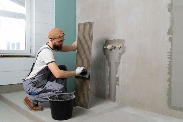 Worker applying gray tile adhesive to a wall in an unfinished room