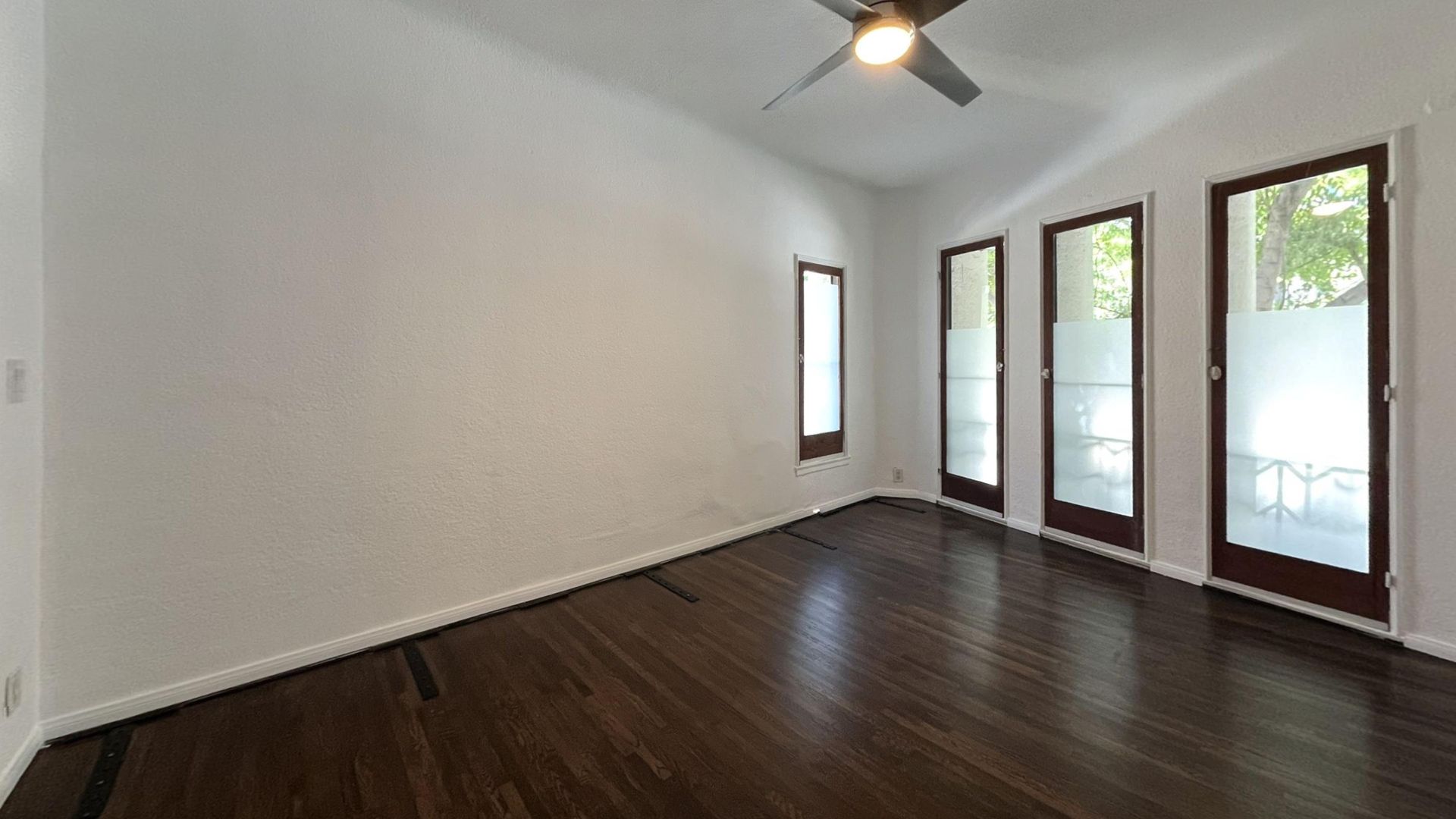 Empty room with dark wood floors, white walls, and three glass doors with frosted glass panels.