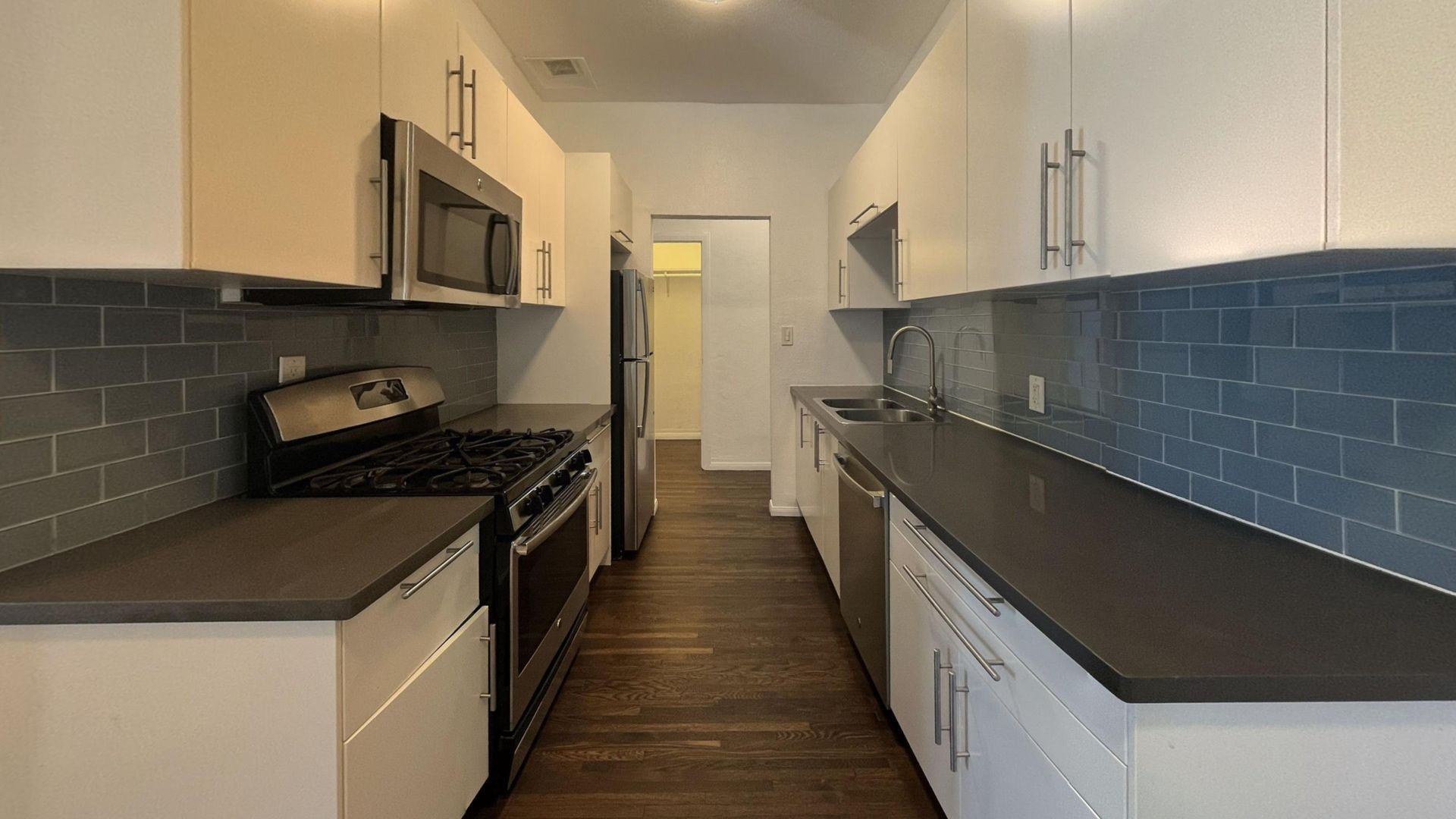 Modern galley kitchen with white cabinets, dark countertops, and stainless steel appliances.