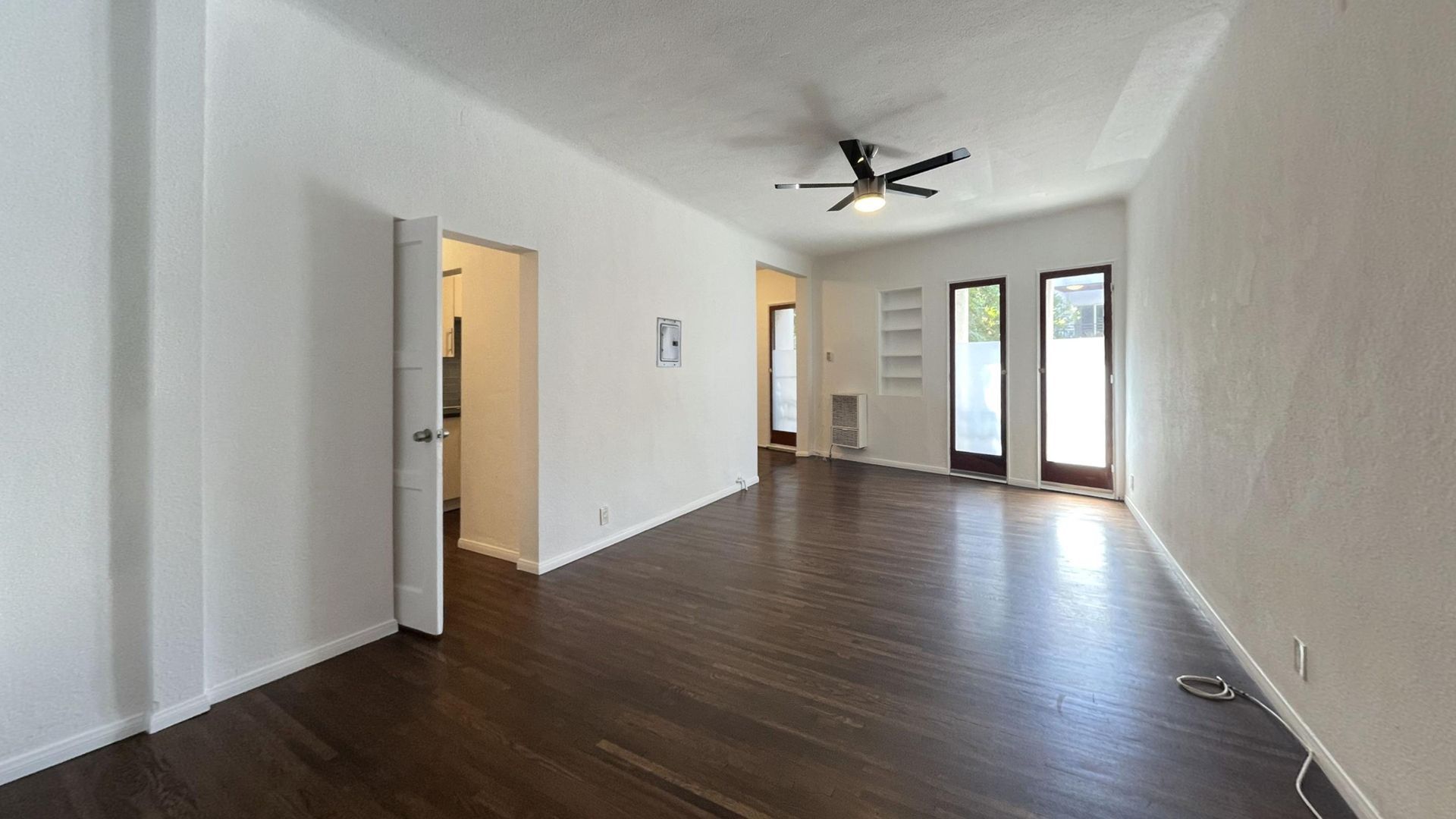Empty living room with dark wood floor, white walls, and three doors leading outside.