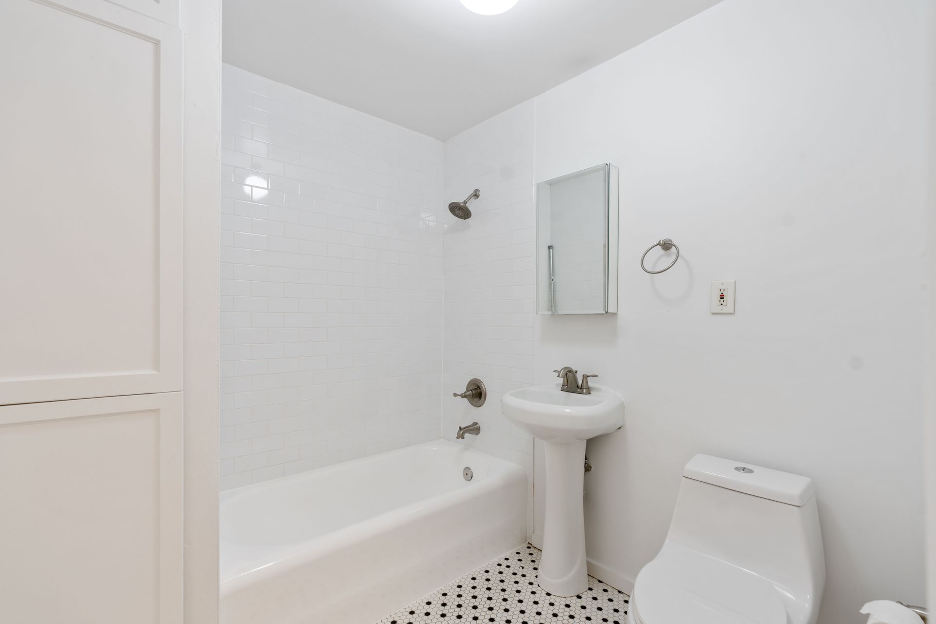 White bathroom with tub, shower, sink, toilet, and black and white patterned floor.