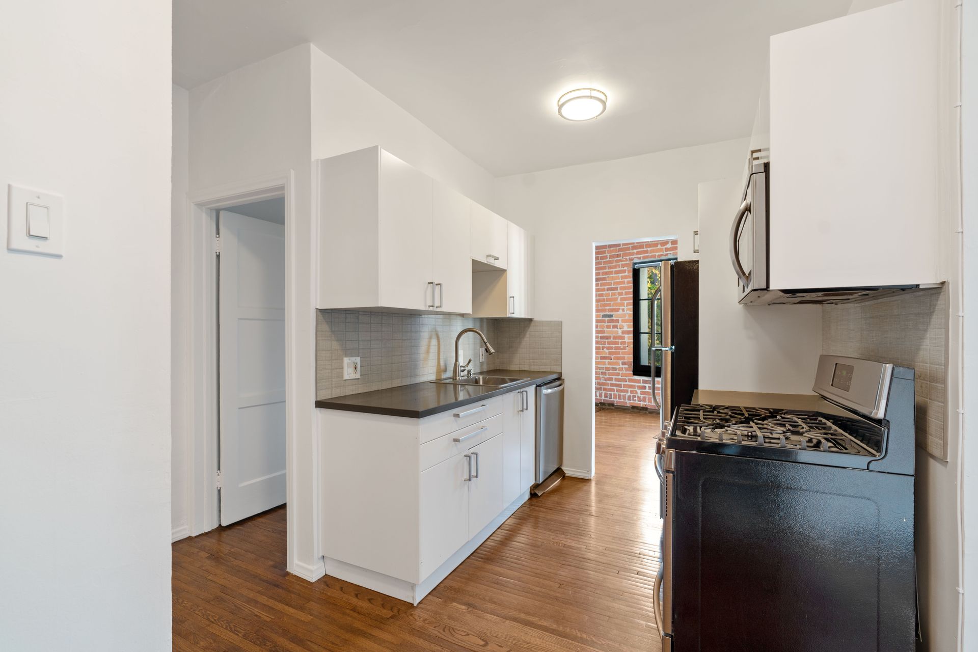 White kitchen with black countertops, stainless steel appliances, and wood flooring.
