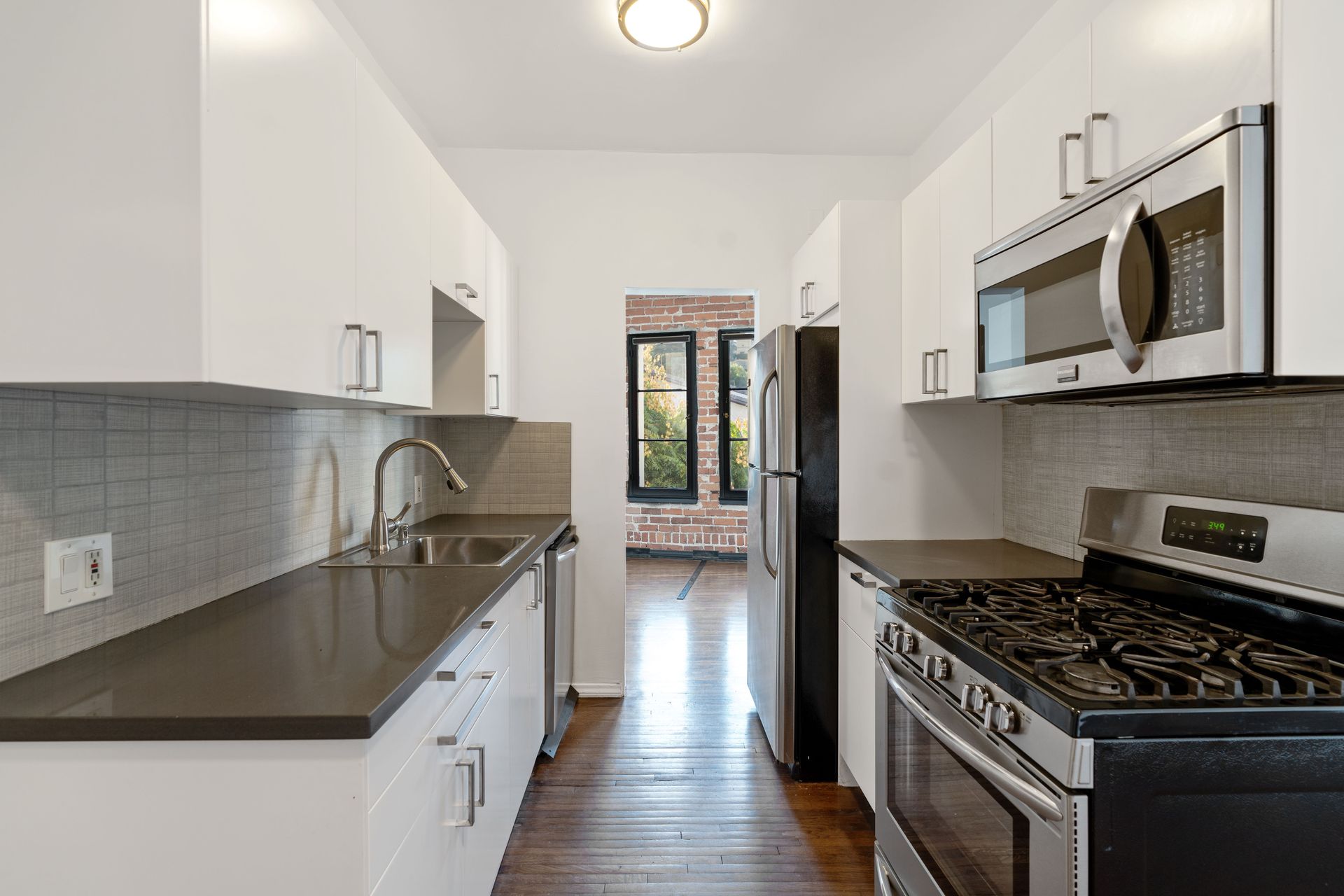 Modern galley kitchen with white cabinets, stainless steel appliances, and dark countertops.