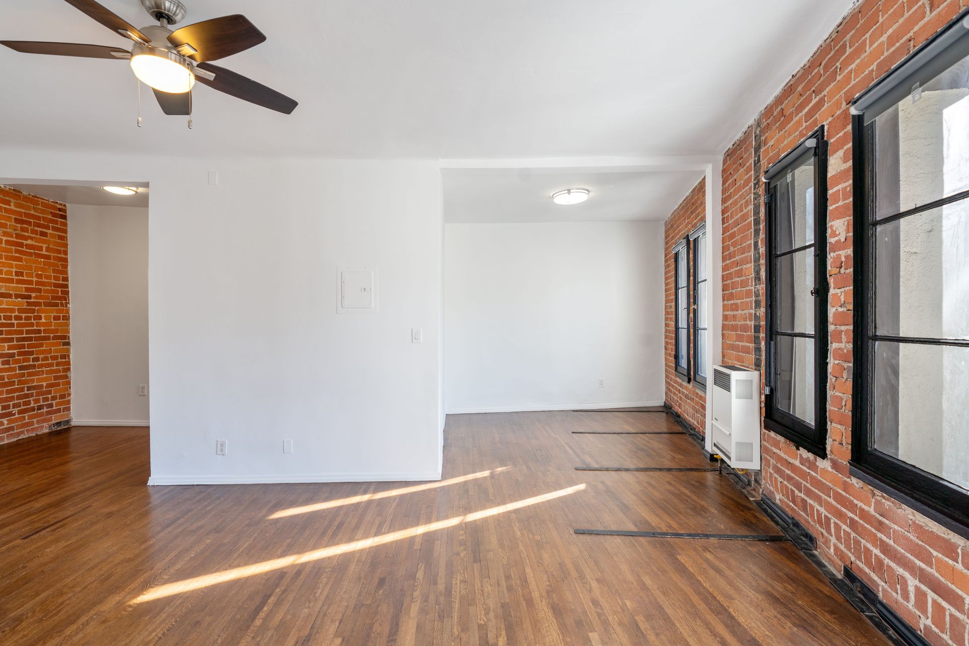 Empty apartment interior with exposed brick walls, windows, and hardwood floors.