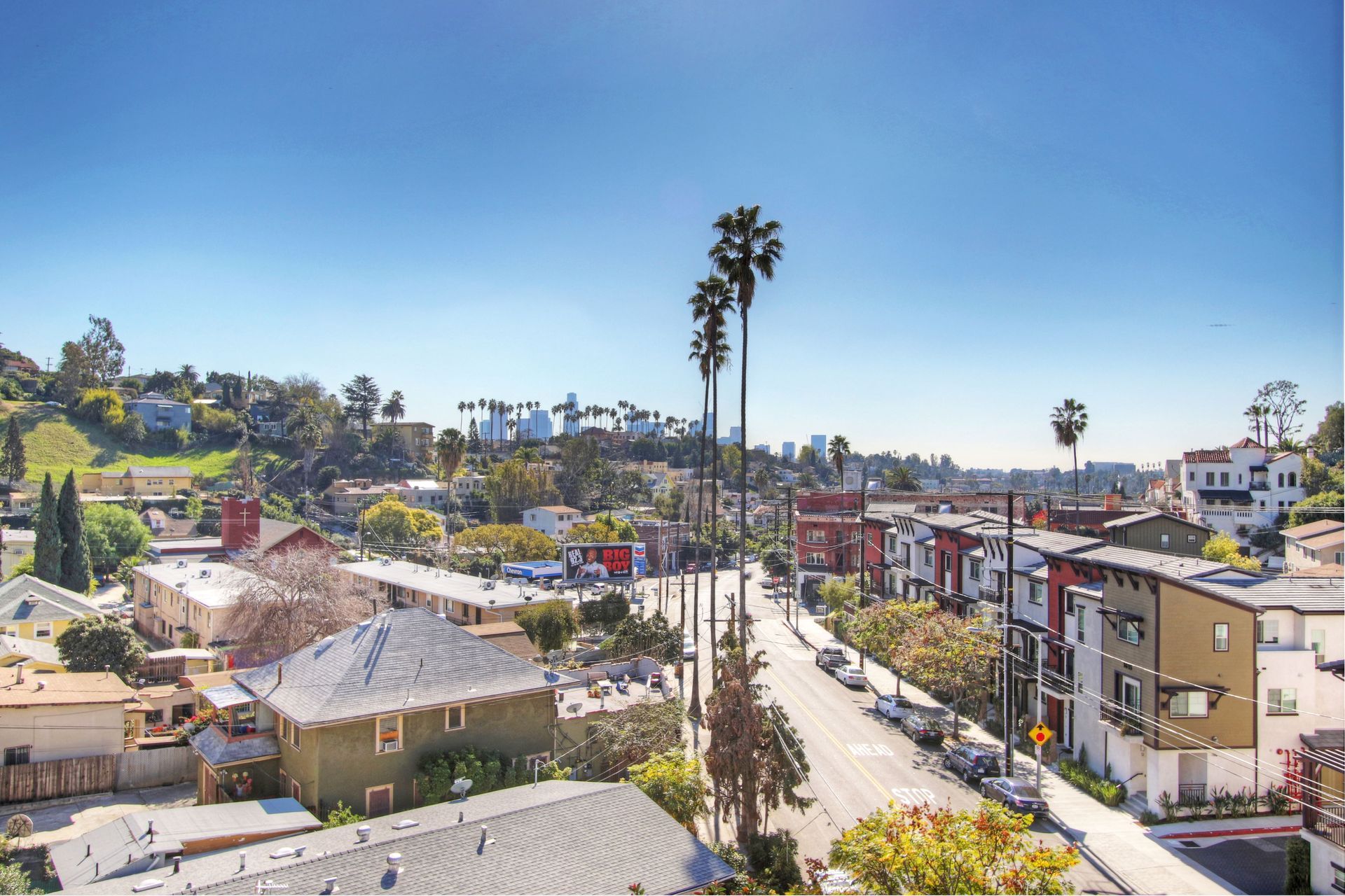 City street with houses, palm trees, and clear blue sky.