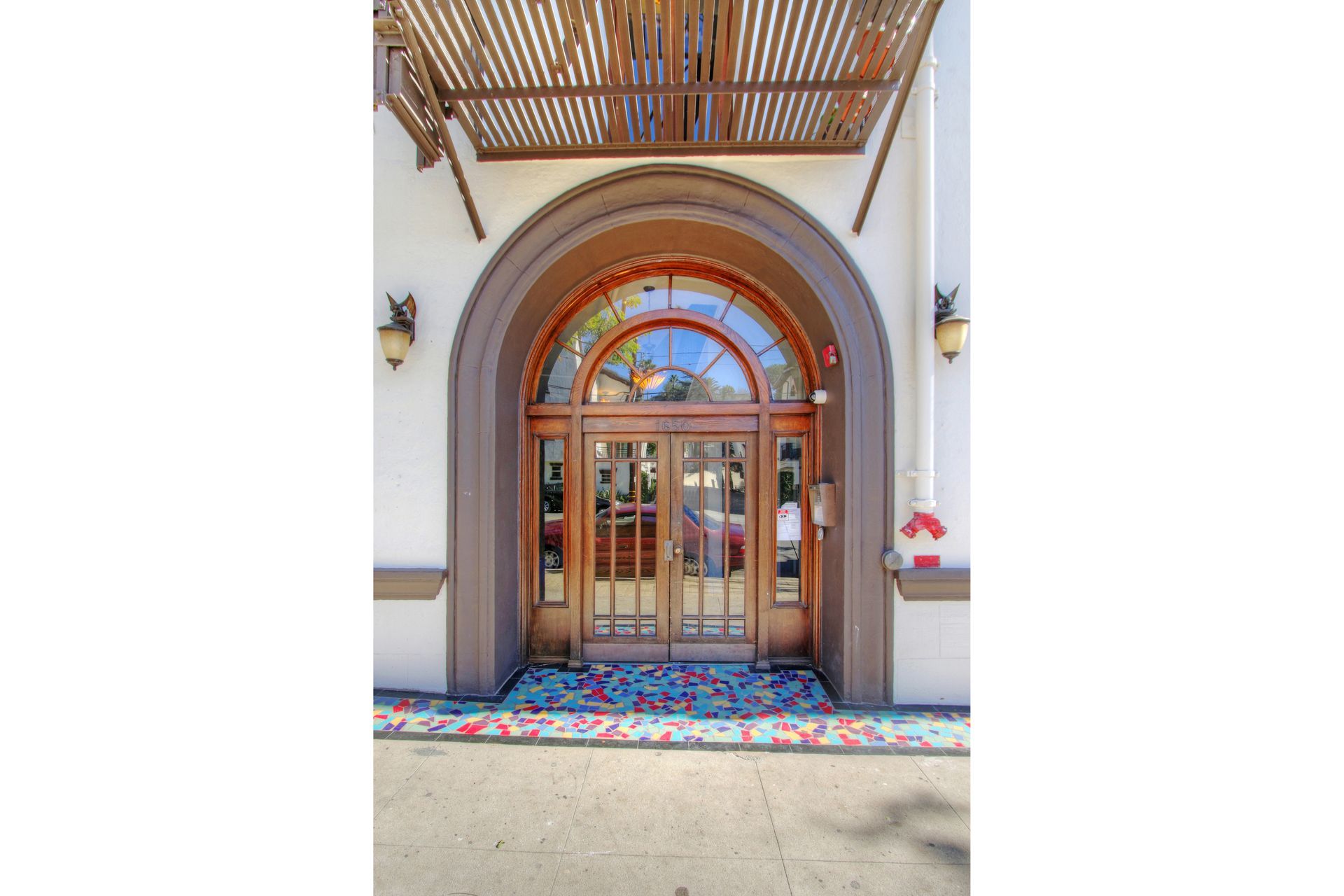 Wooden arched doorway with glass and mosaic floor inlay. Brown and white building facade.