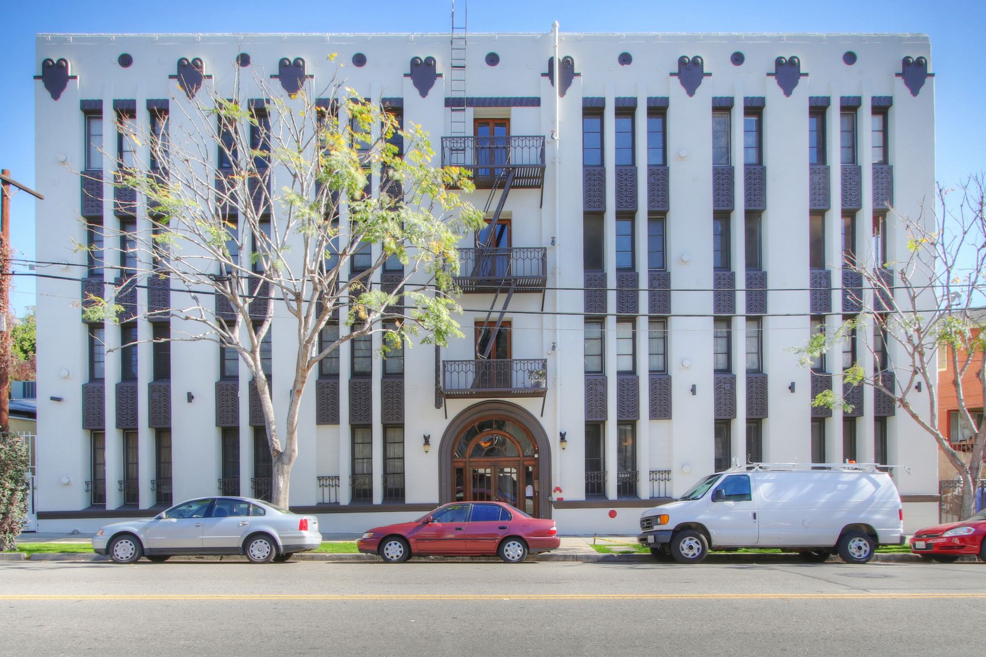 White apartment building with dark blue decorative elements and a red car parked out front.