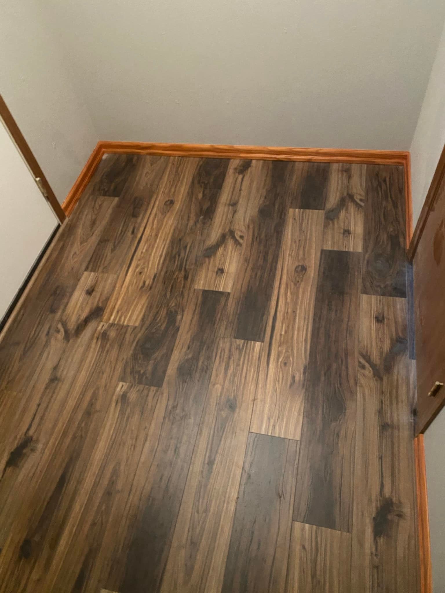 Wood-look laminate flooring in a small, narrow room with brown trim along the walls.
