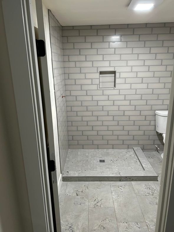 Bathroom with gray tile walls and floor, shower niche, and toilet visible.