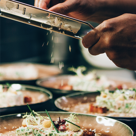 Een persoon die kaas raspt op een bord met eten