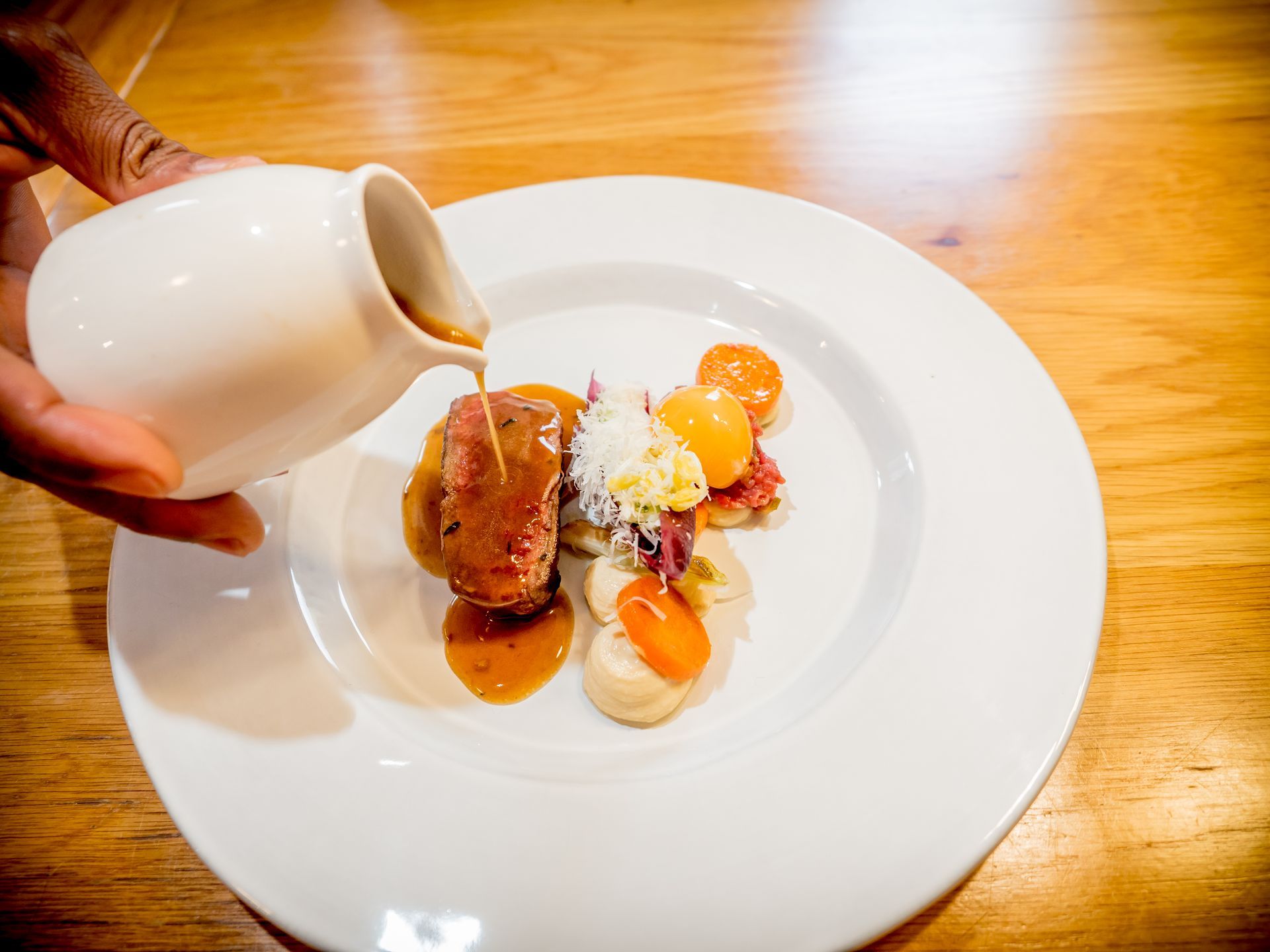 Iemand giet saus over een bord eten.