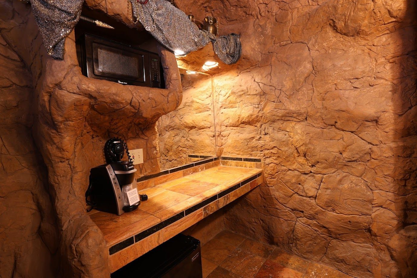 A kitchen in a cave with a microwave and a coffee maker.