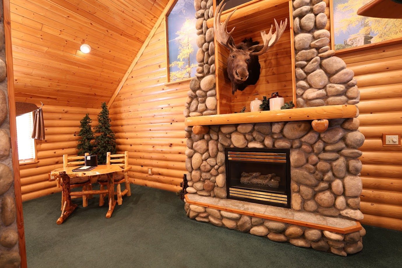 A log cabin with a stone fireplace and a moose head on the wall.