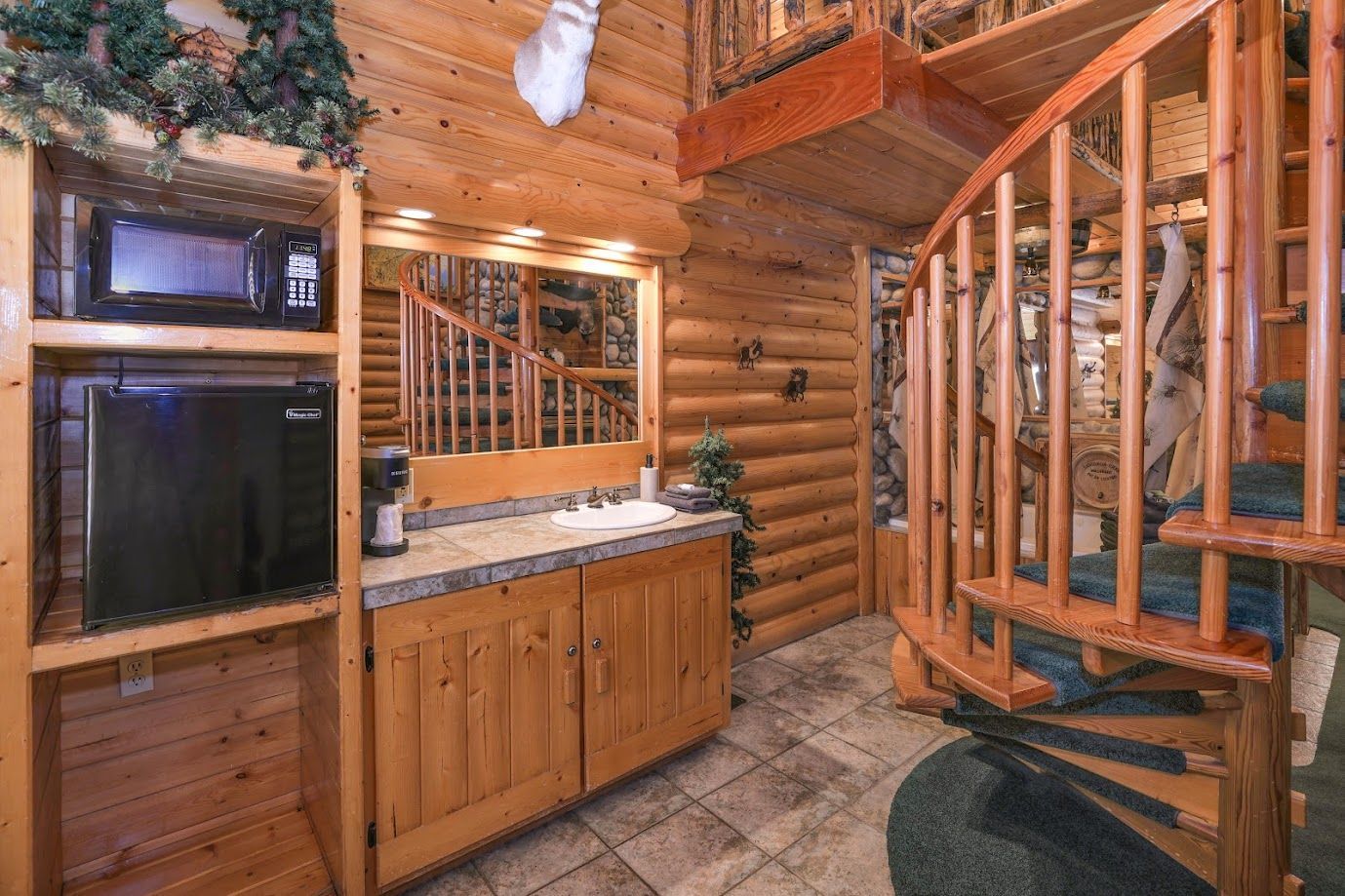 A kitchen in a log cabin with a spiral staircase leading to the second floor.