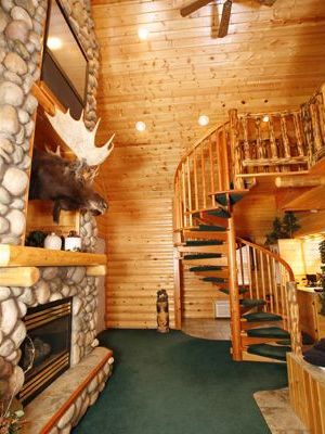 A log cabin with a moose head on the fireplace and a spiral staircase