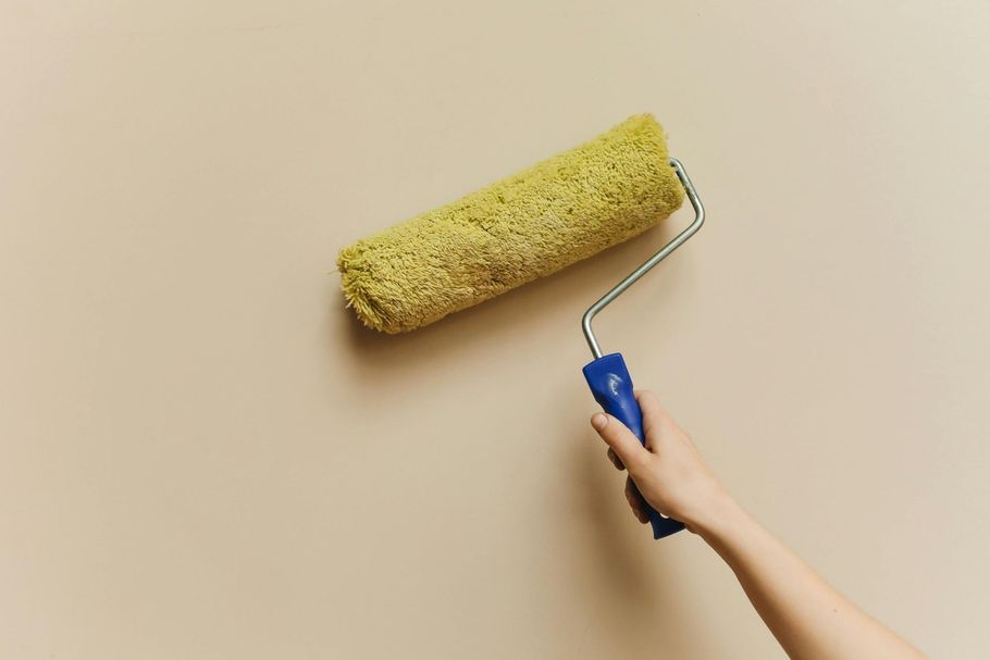 A person holds a yellow paint roller against a light-colored wall.
