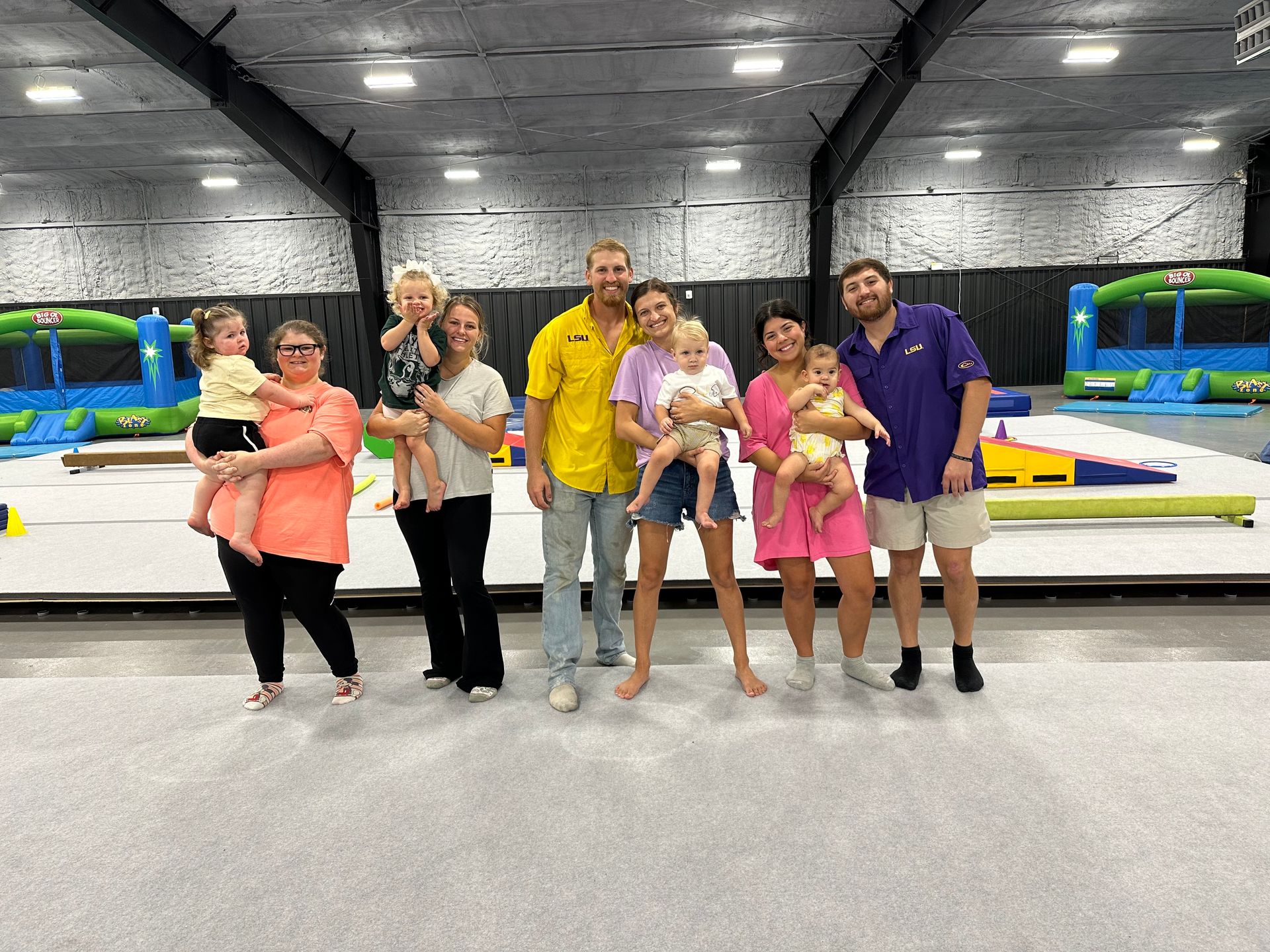 A woman in yellow lies on her back, holding a laughing baby in the air during an exercise class.