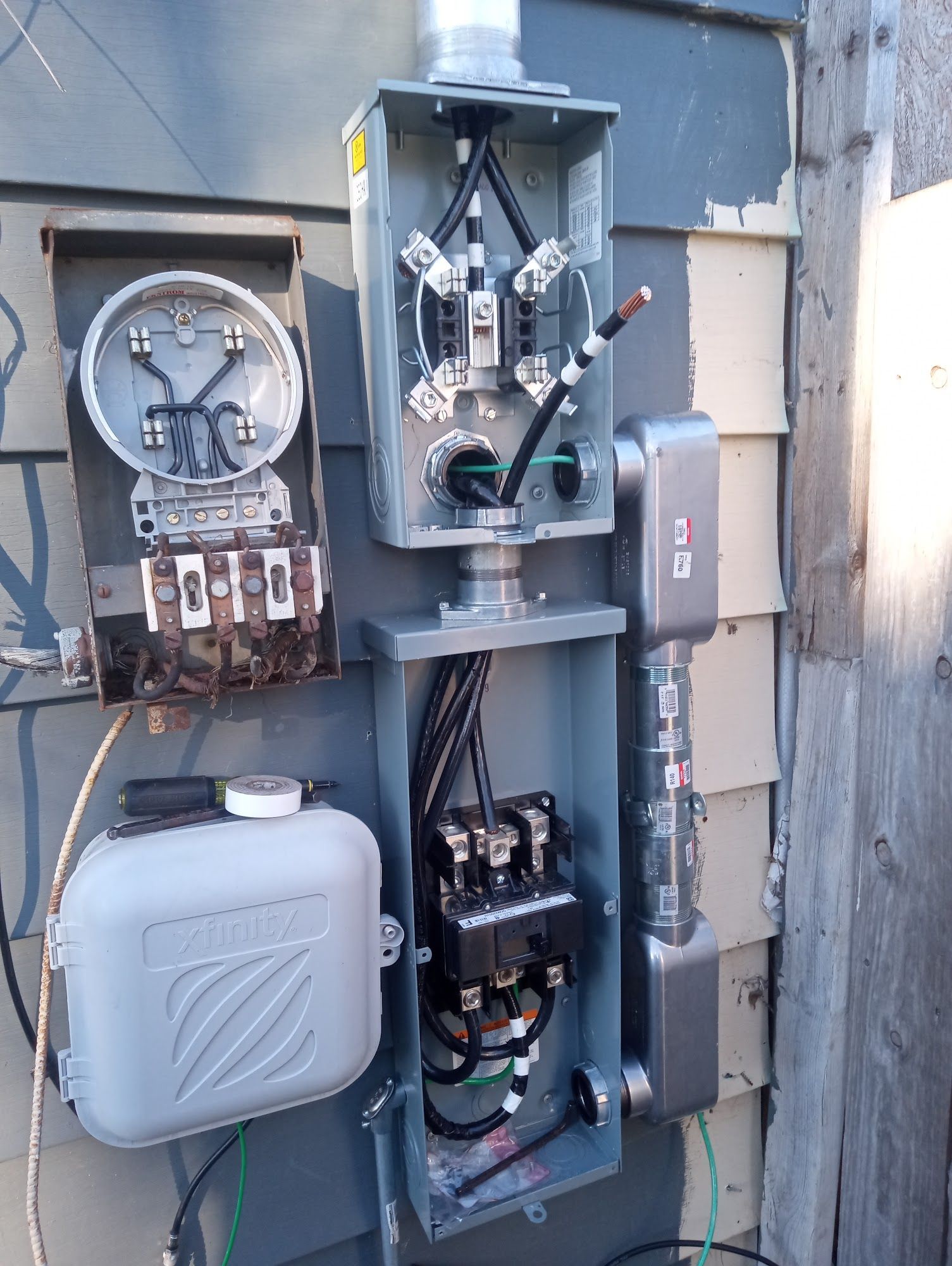 Electrical meter panel with conduit, wires, and junction boxes on a weathered building exterior.