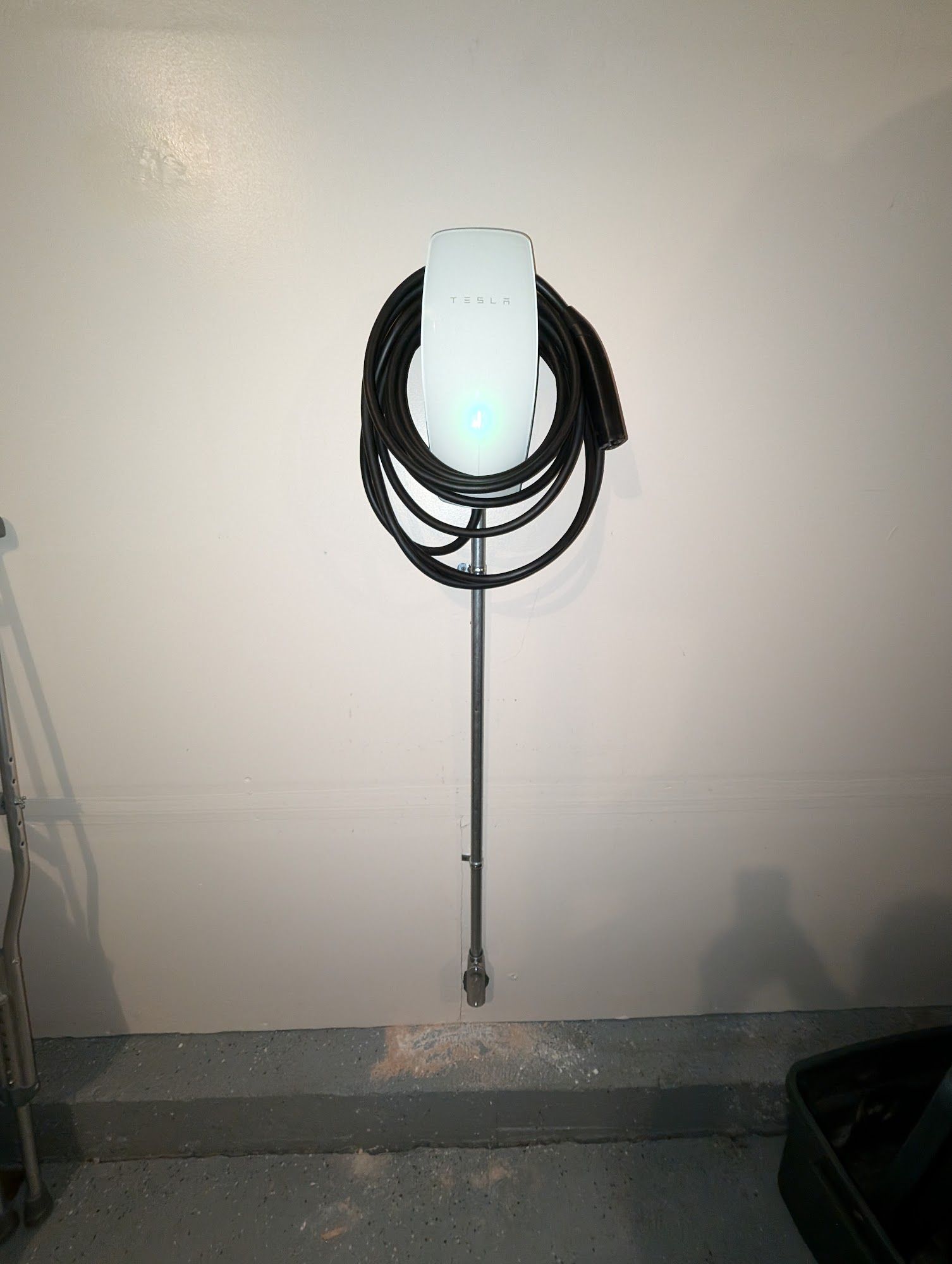 Wall-mounted Tesla charger with coiled black cable, on a white wall, in a garage setting.