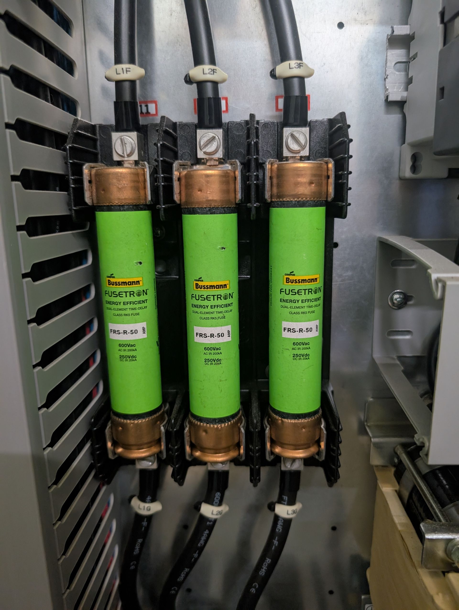 Three green fuses in a metal electrical panel, each with black wires connected.