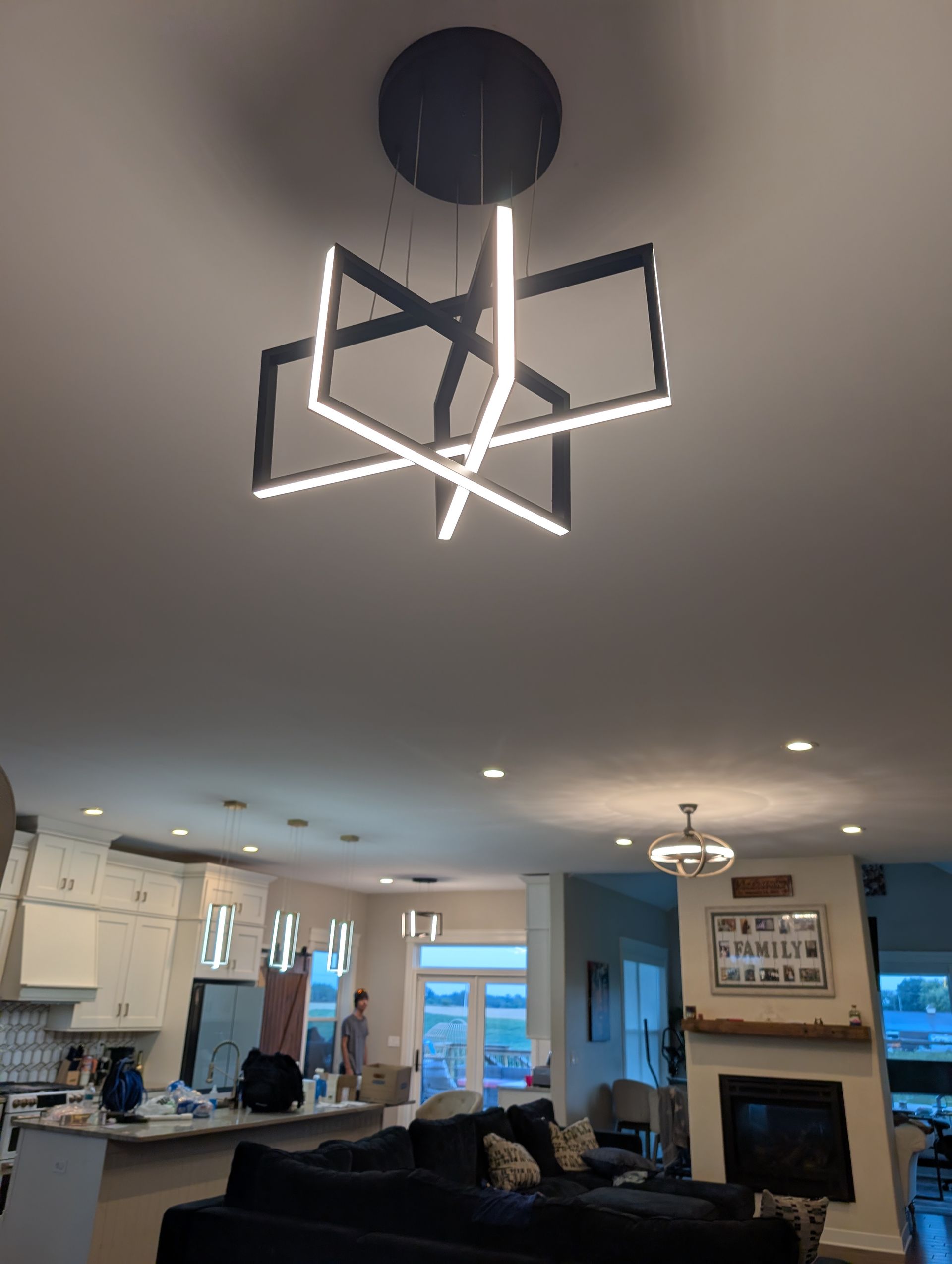 Modern geometric chandelier in a living room with open kitchen and fireplace.