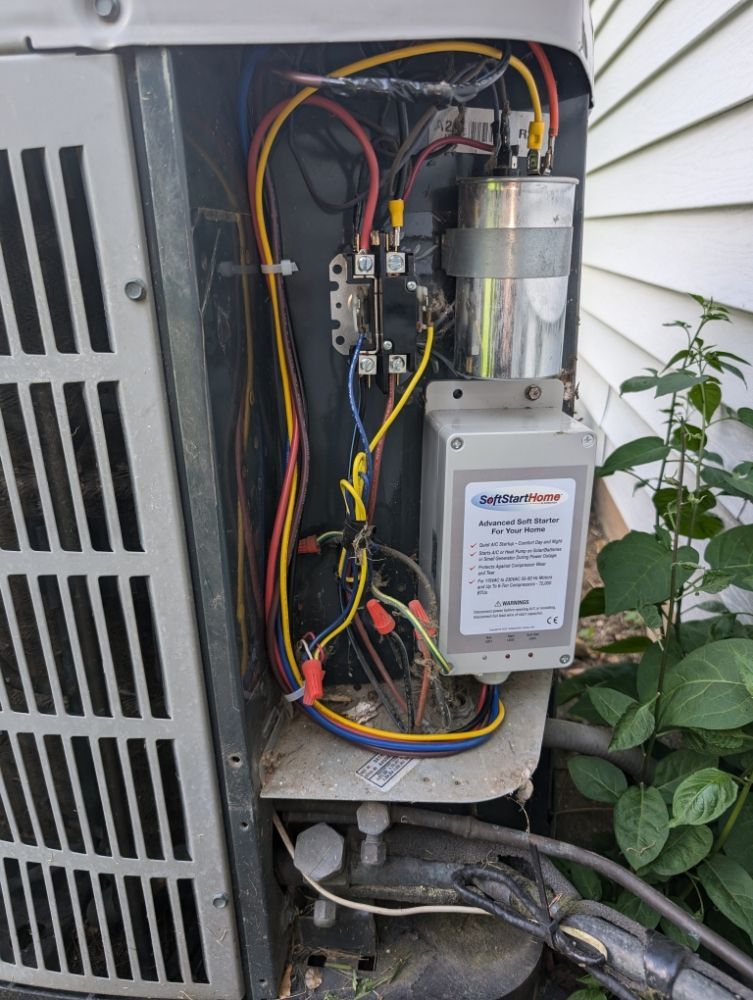 Open view of an outdoor AC unit's electrical components. Wires in various colors connect to a capacitor and other parts.