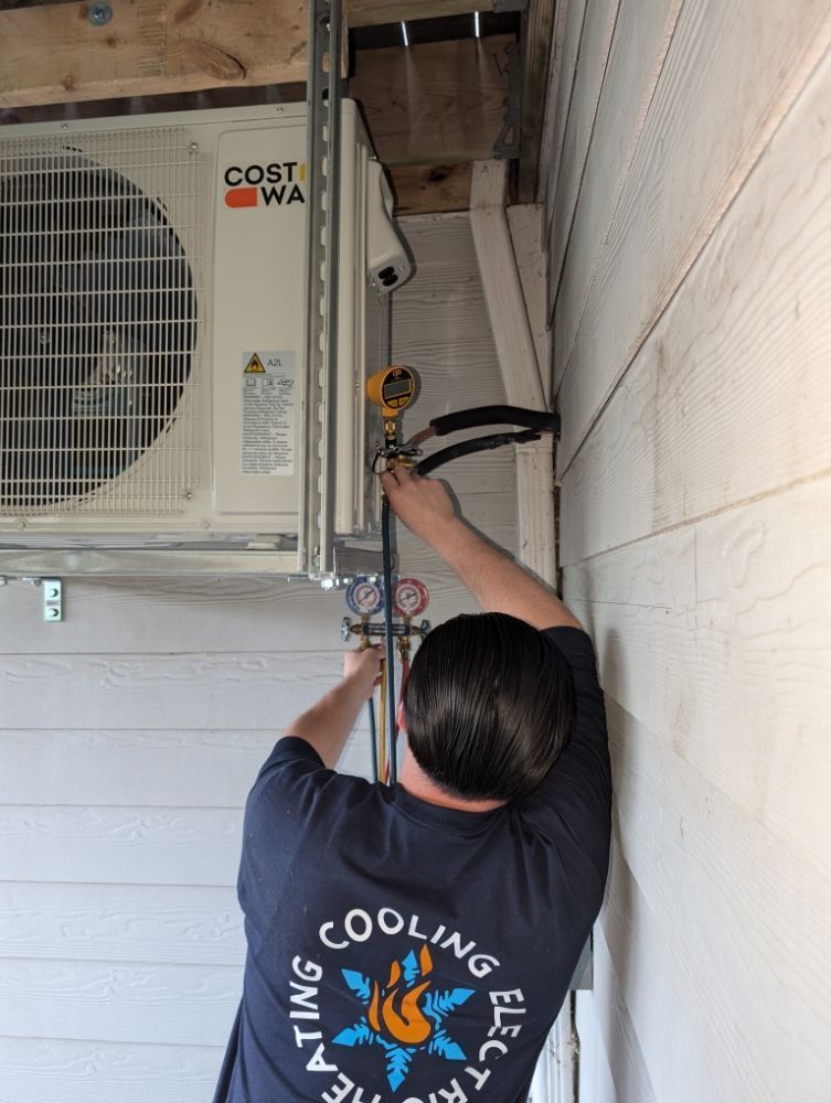 HVAC technician working on an outdoor air conditioning unit. He is connecting gauges. The building has white siding.