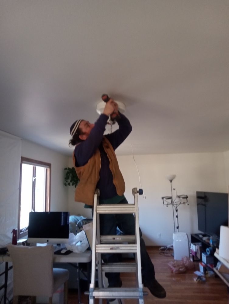 Person on a ladder installing a light fixture on a white ceiling in a room.