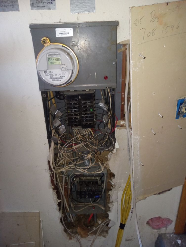 Electrical panel, exposed wires, in a wall, meter attached.