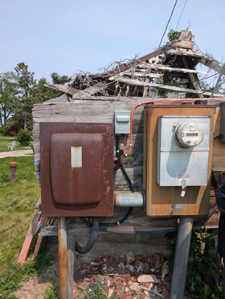 Rusty electrical boxes and meter on a dilapidated wooden structure.