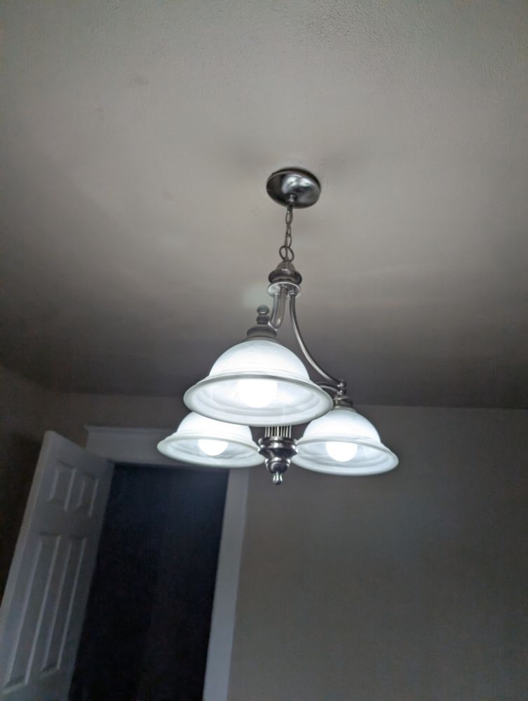Three-light chandelier with white glass shades hanging from a white ceiling.