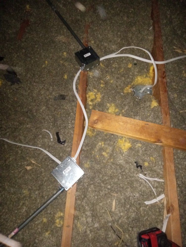 Electrical junction boxes and wiring in an attic, positioned between wooden beams.