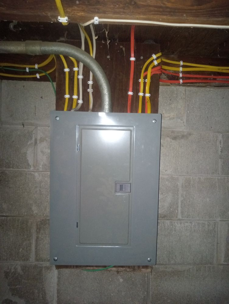 Gray electrical panel on a concrete block wall, with wiring running above.