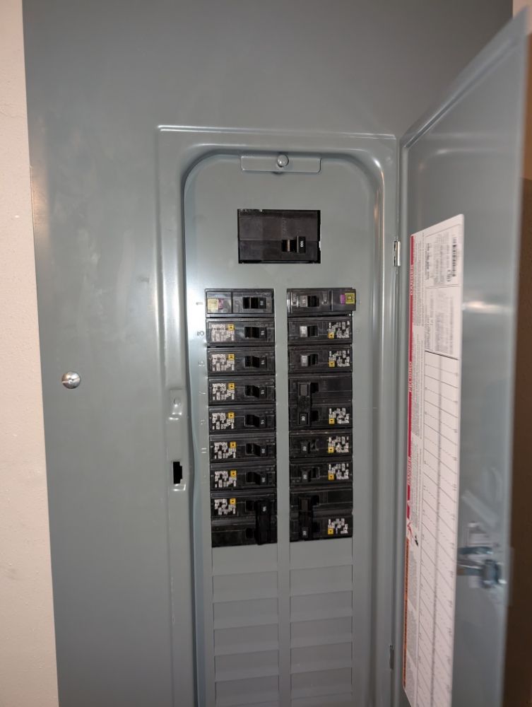 Open electrical panel, gray metal box with circuit breakers. A schedule is on the inside door.