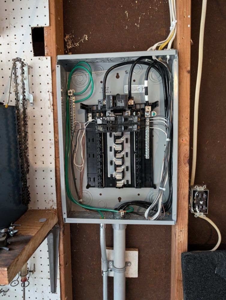 Open electrical panel in a garage, with wires and circuit breakers visible.