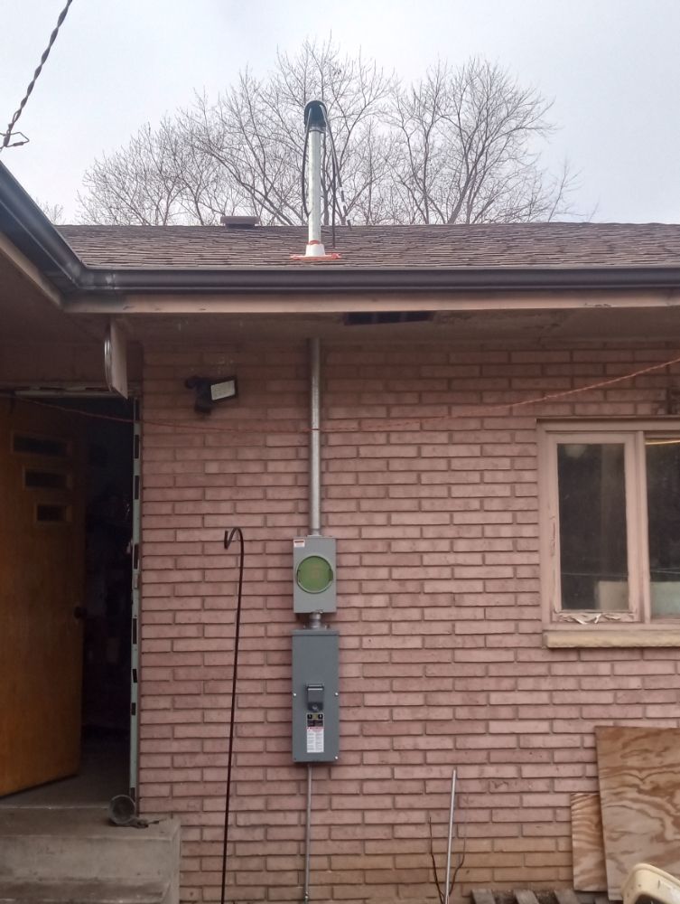 Exterior view of brick building with chimney and electrical panel. Gray metal box on wall; gray conduit.