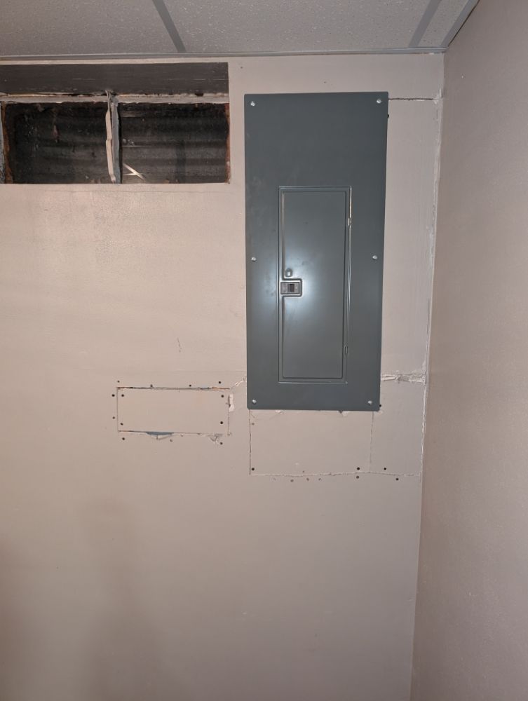 Electrical panel on a white wall with a basement window above.