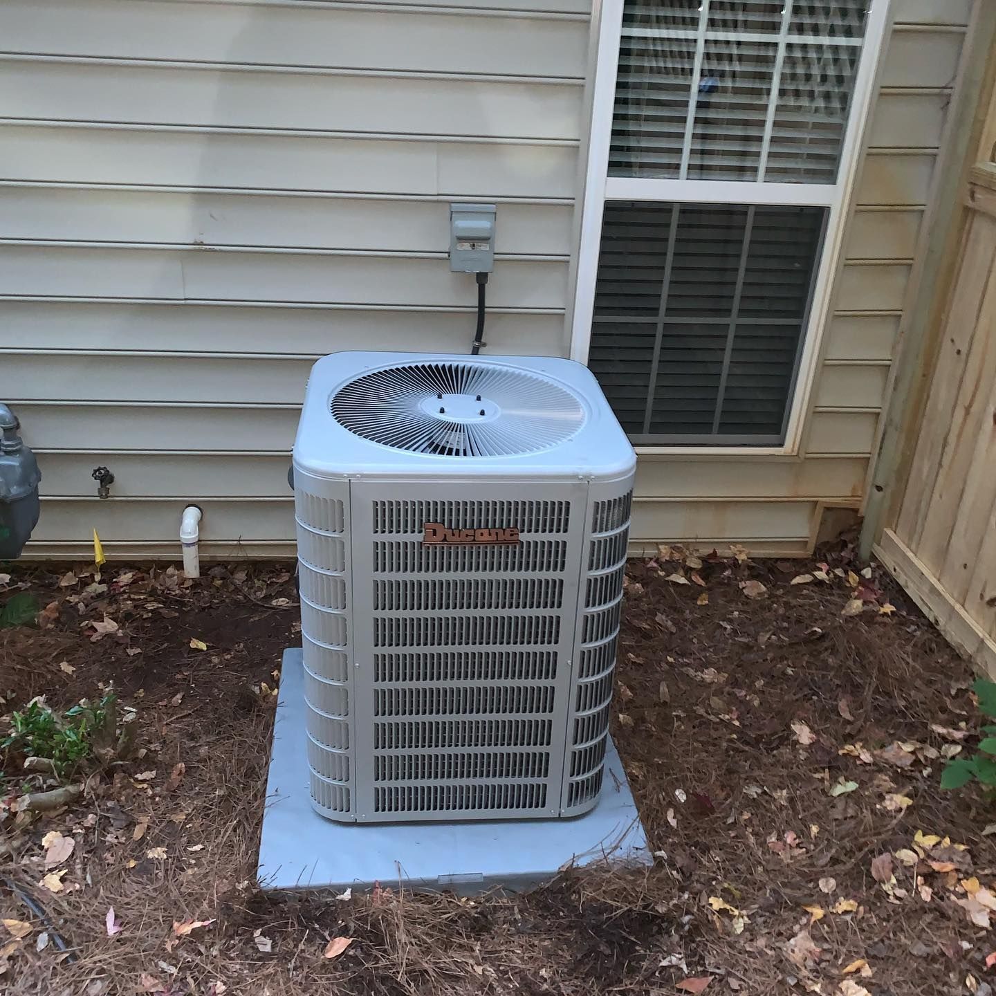 An air conditioner sits outside of a house next to a window