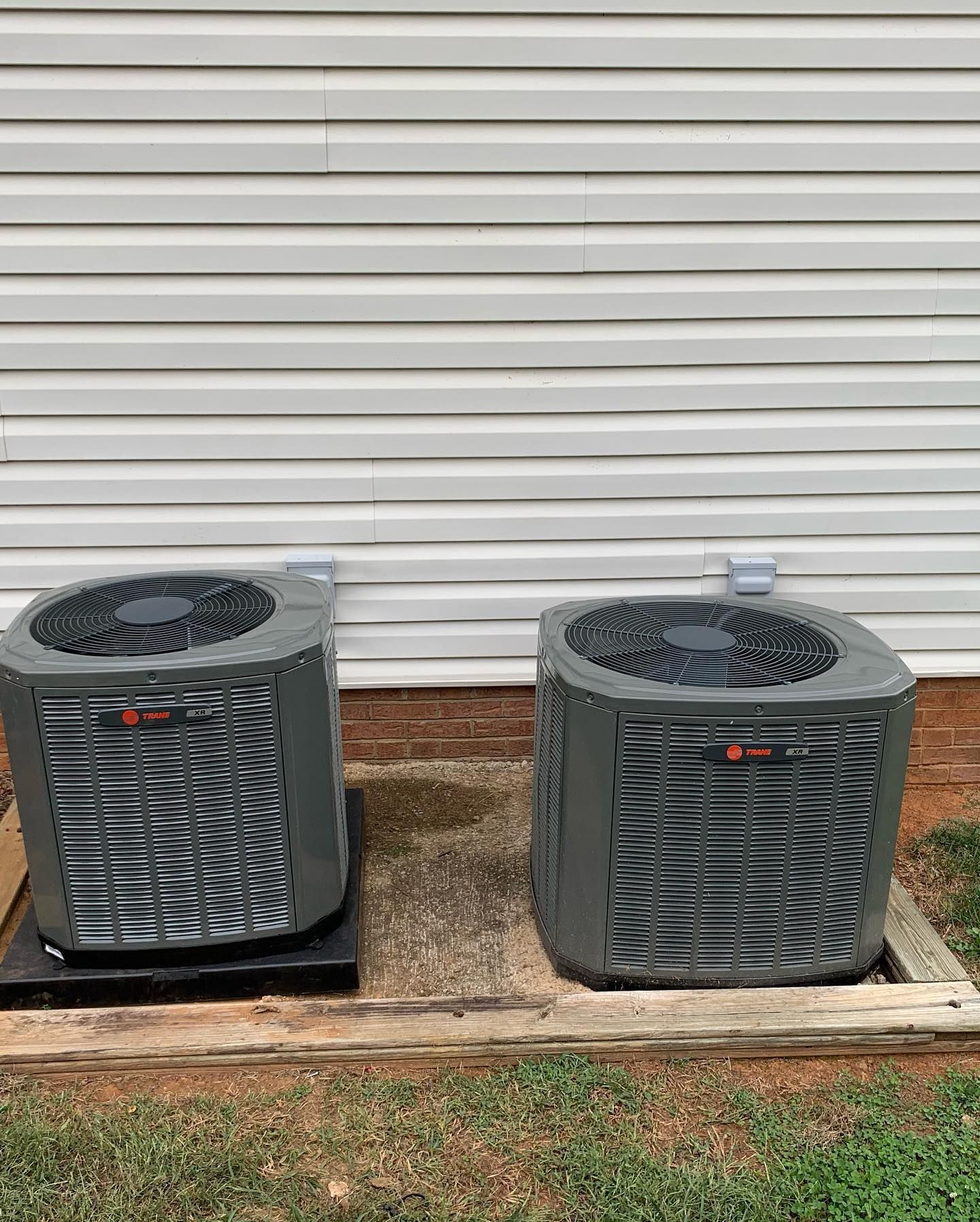 Two air conditioners are sitting on a wooden pallet in front of a house.