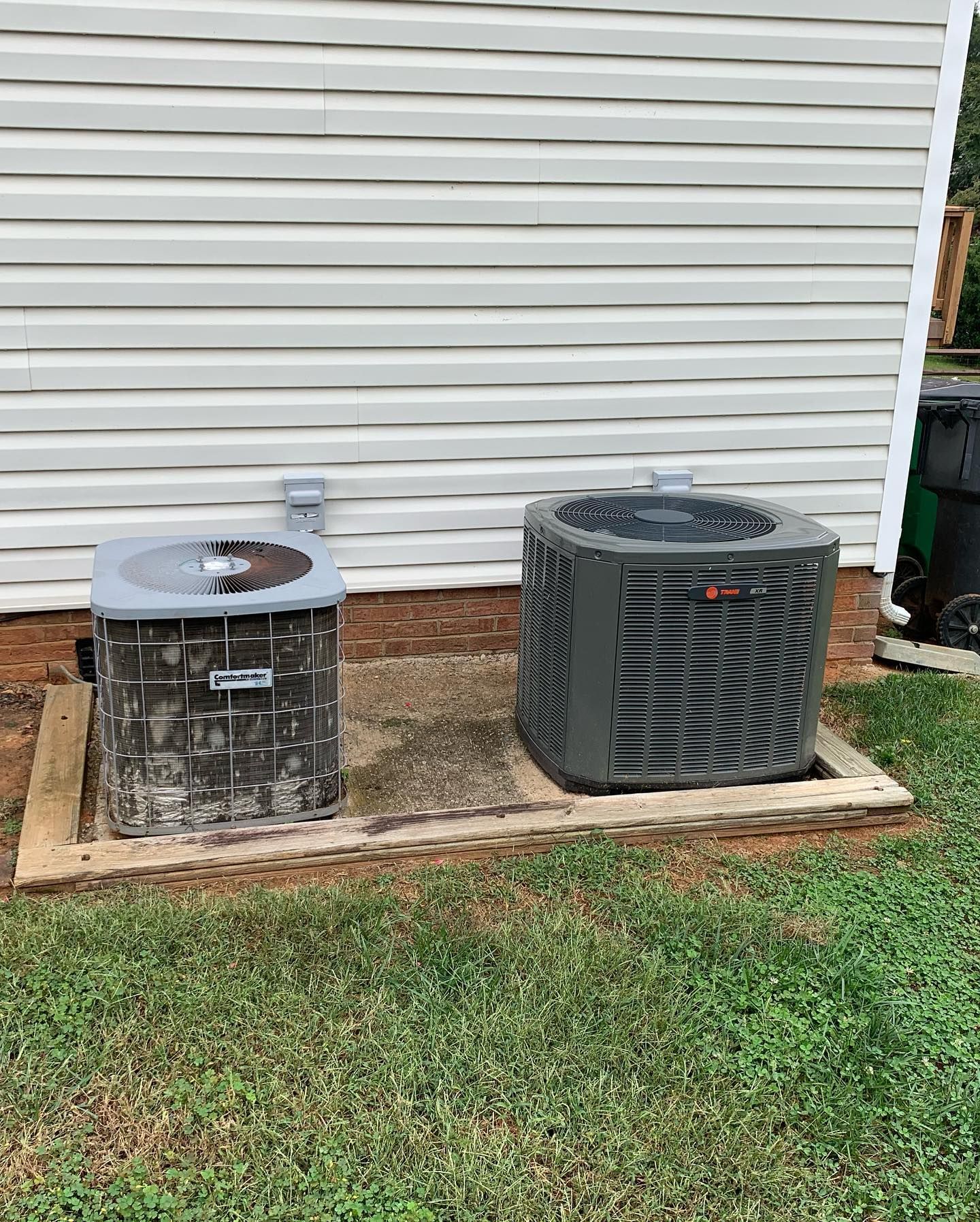 Two air conditioners are sitting next to each other in front of a house.