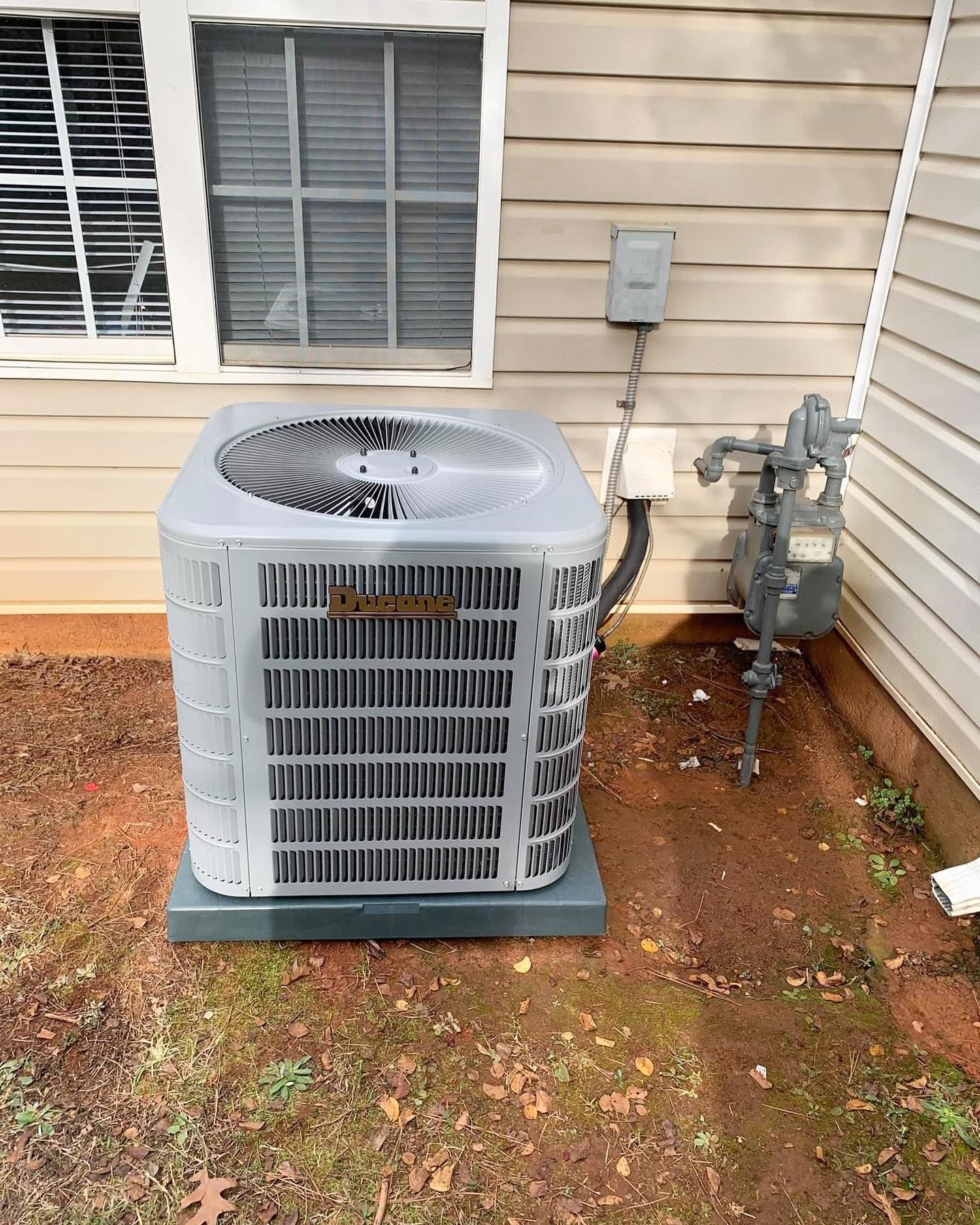 An air conditioner is sitting outside of a house next to a window.
