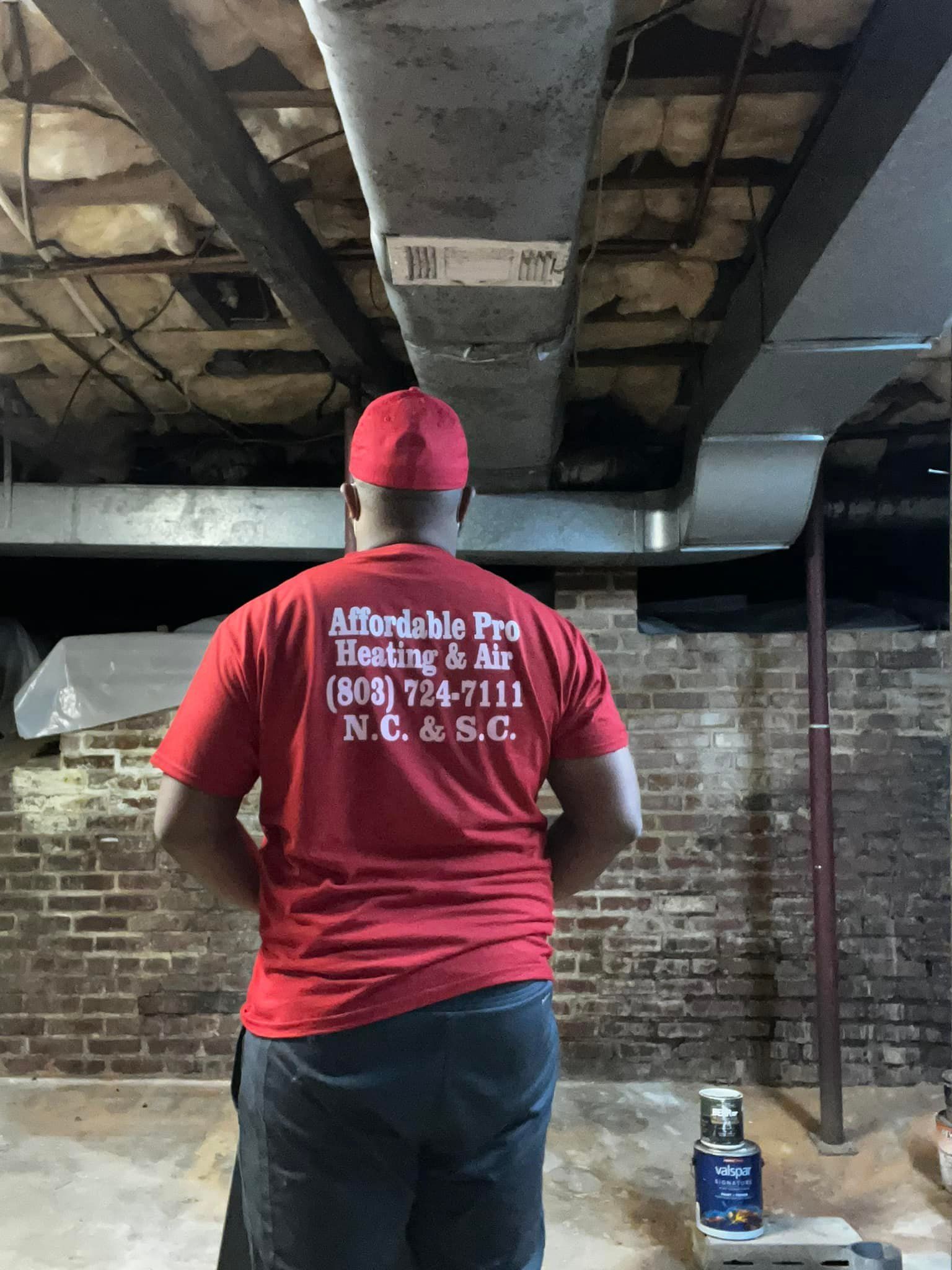 A man in a red shirt is standing in front of a brick wall.