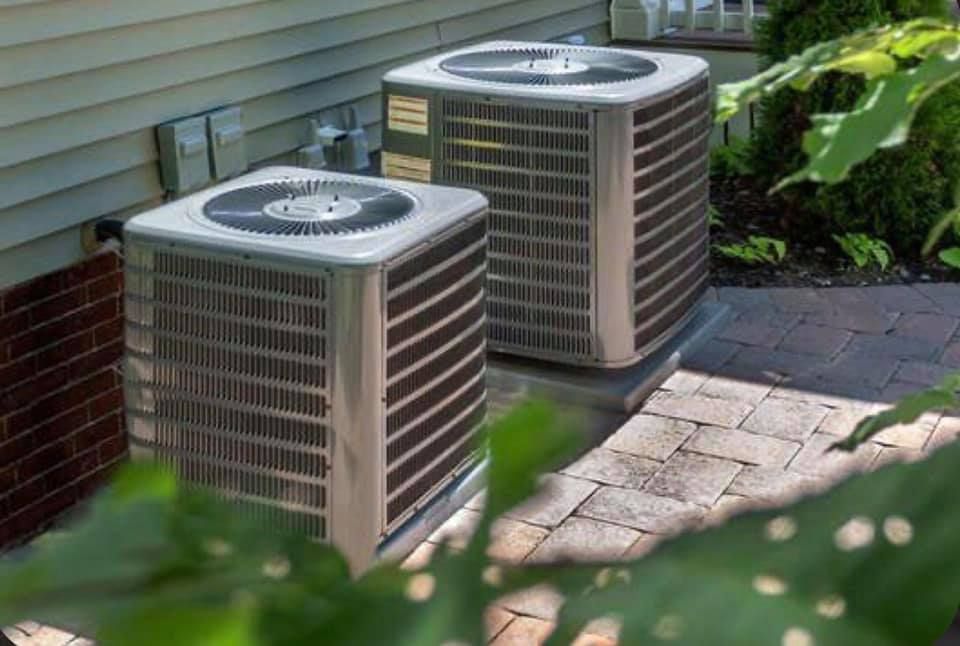 Two air conditioners are sitting on the side of a house.