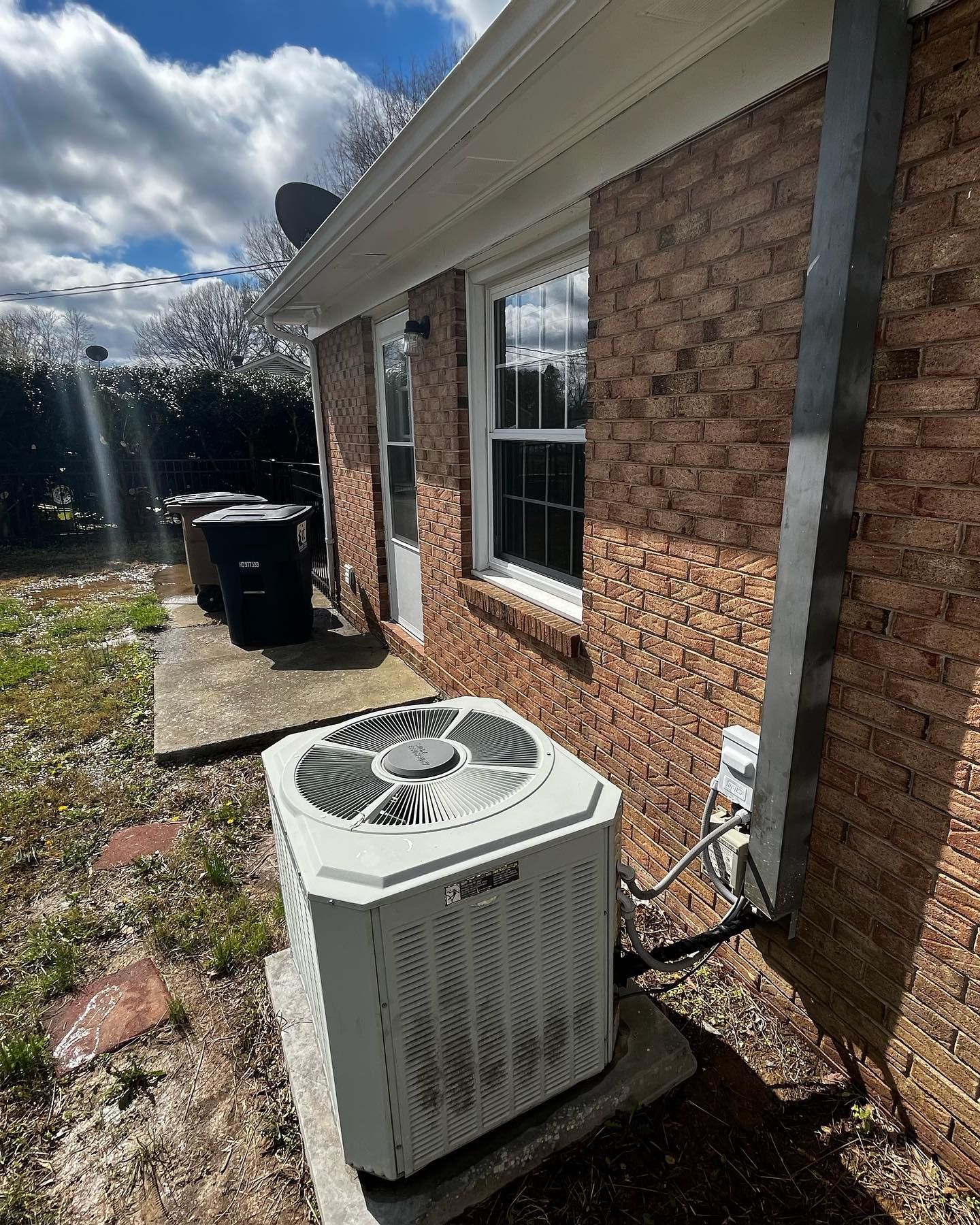 A white air conditioner is sitting on the side of a brick house.