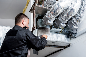 A man is working on a ventilation system in a building.