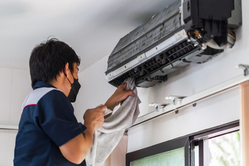 A man wearing a mask is cleaning an air conditioner with a towel.